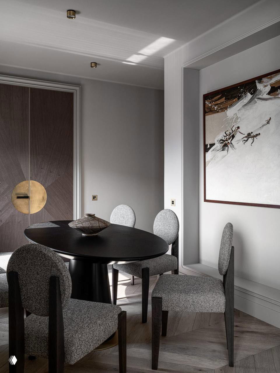 Столовая зона в проекте 140 м²: тёмный круглый стол и обитые серой тканью стулья на фоне декоративной двери с латунной вставкой.