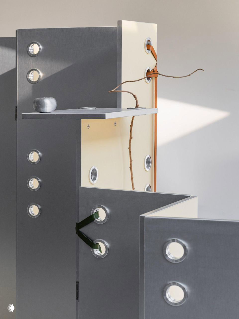 Крупный план угловых панелей и перегородок с круглыми окнами и кожаными элементами, часть композиции напоминает заострённые листы и стебли растений.