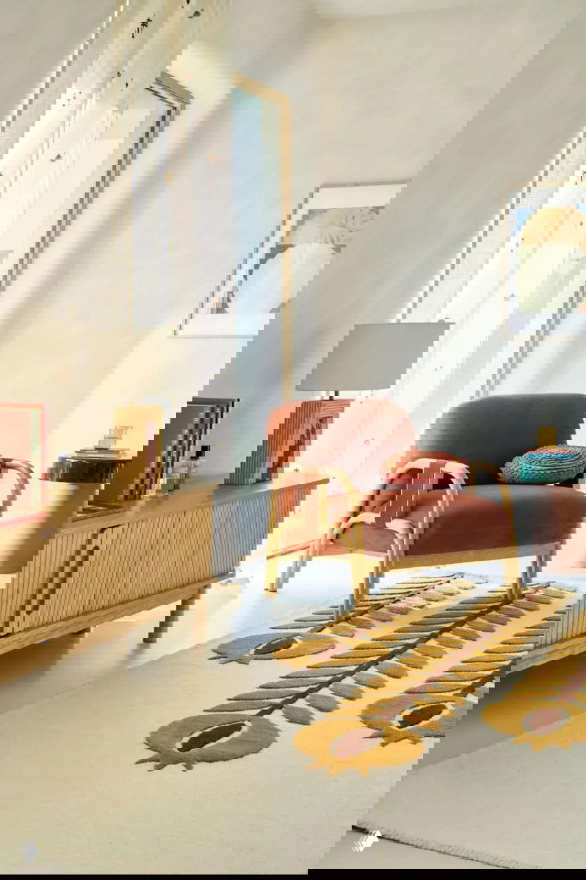 Уютный уголок с креслом в терракотовом бархате, низким комодом из светлого дерева и ковром с графическим растительным мотивом в духе 1970‑х.