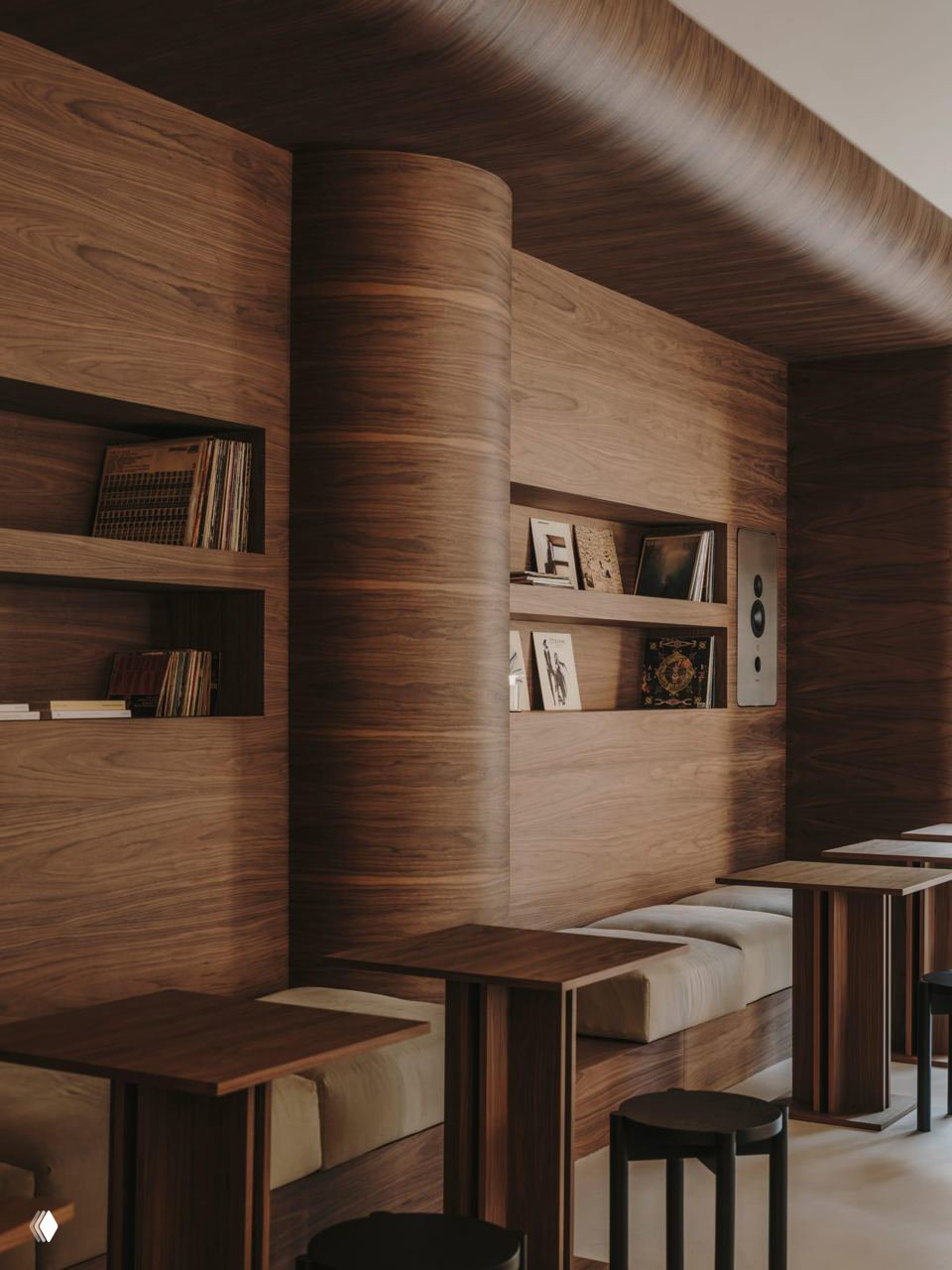 Интерьер кафе с тёплой древесной облицовкой: изогнутые панели, встроенные сиденья и небольшие столики рядом с полками с виниловыми пластинками.