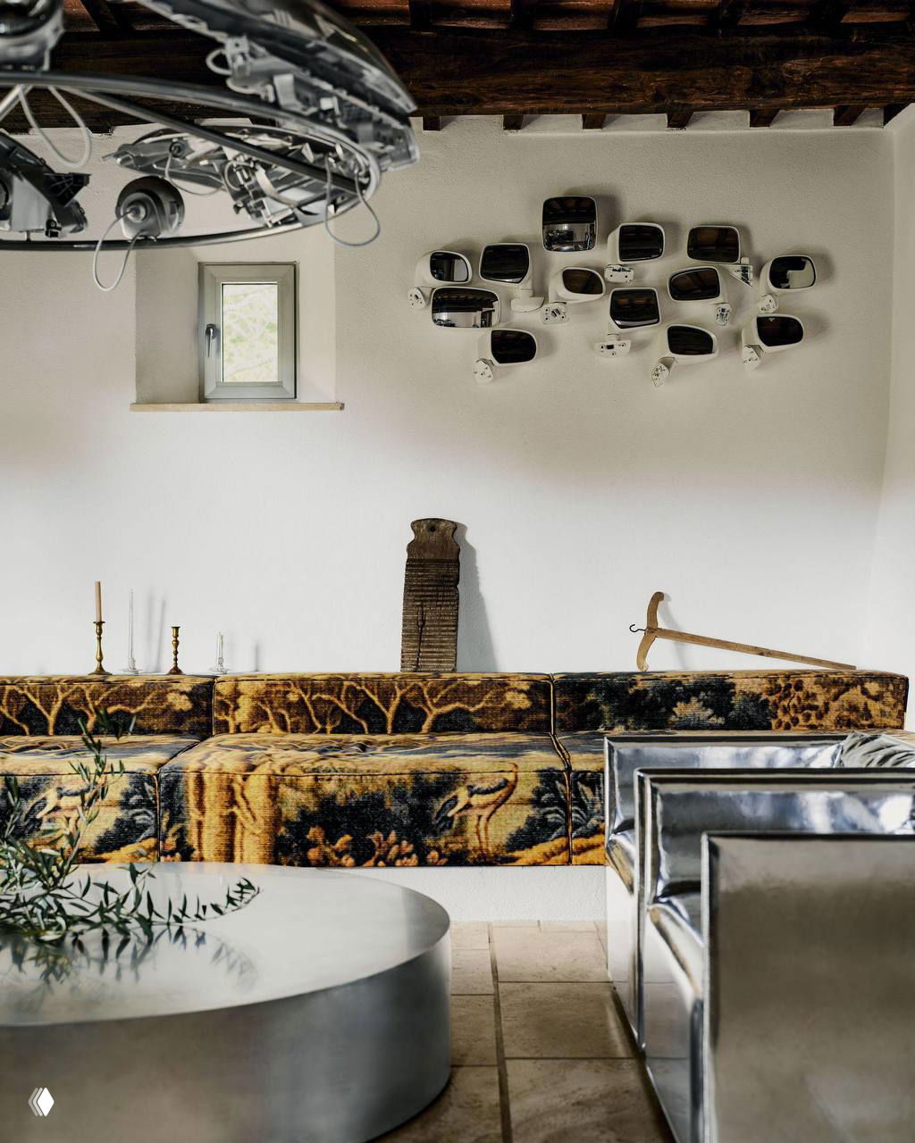 Гостиная с низким диваном в орнаменте и настенной инсталляцией из зеркал заднего вида: сочетание винтажных и индустриальных деталей.