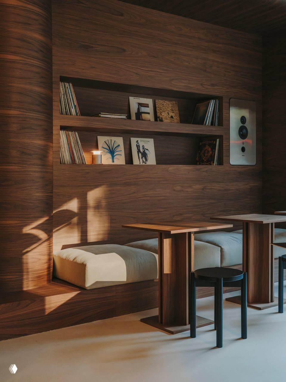 Полка с виниловыми пластинками и декором на фоне тёплой деревянной облицовки; видны встроенные акустические модули и мягкие сиденья у столиков.