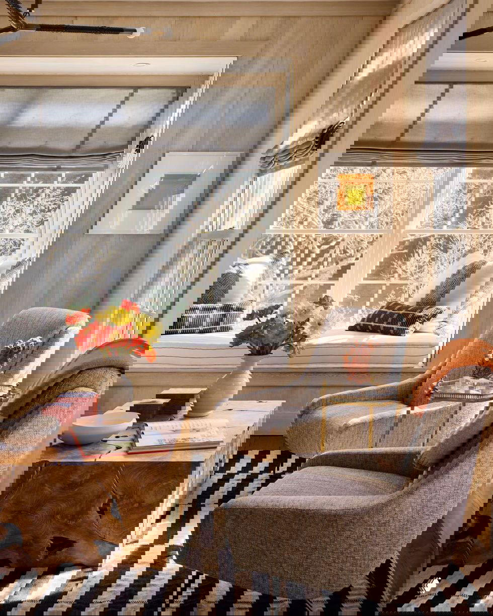 Светлая зона у окна с подушками на подоконнике, креслами и деревянным журнальным столом — натуральные материалы и естественное освещение.