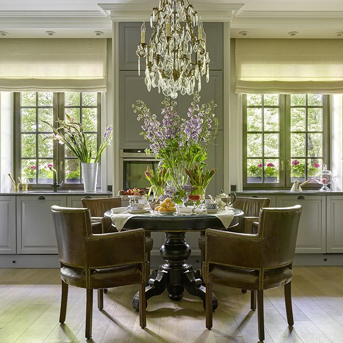Кухонно-обеденная зона с большим овальным столом, зелёными аксессуарами и классической люстрой над центром — пример сочетания классики и практичности.