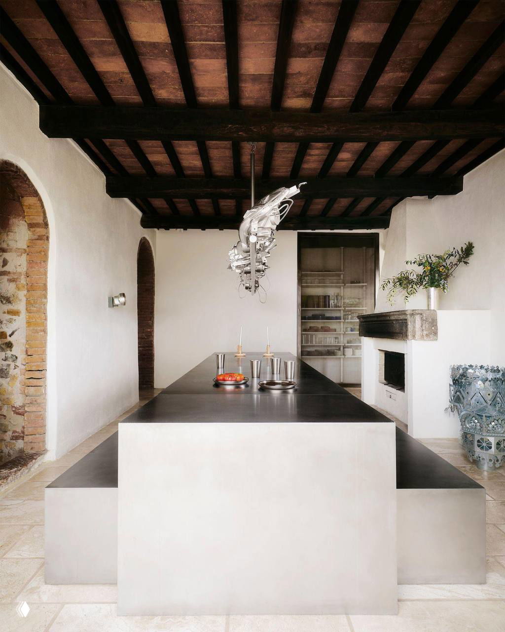 Длинный обеденный стол из нержавеющей стали в просторной столовой с деревянными балками на потолке и оригинальным светильником из автомобильных фар.