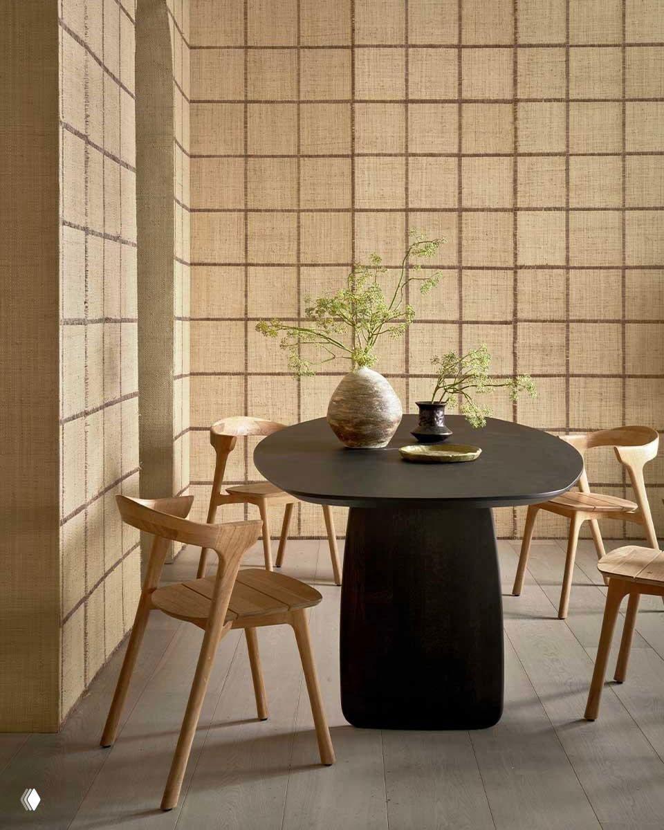 Обеденная зона с круглым тёмным столом и легкими деревянными стульями на фоне стен с текстильной фактурой — минимализм и природная палитра.