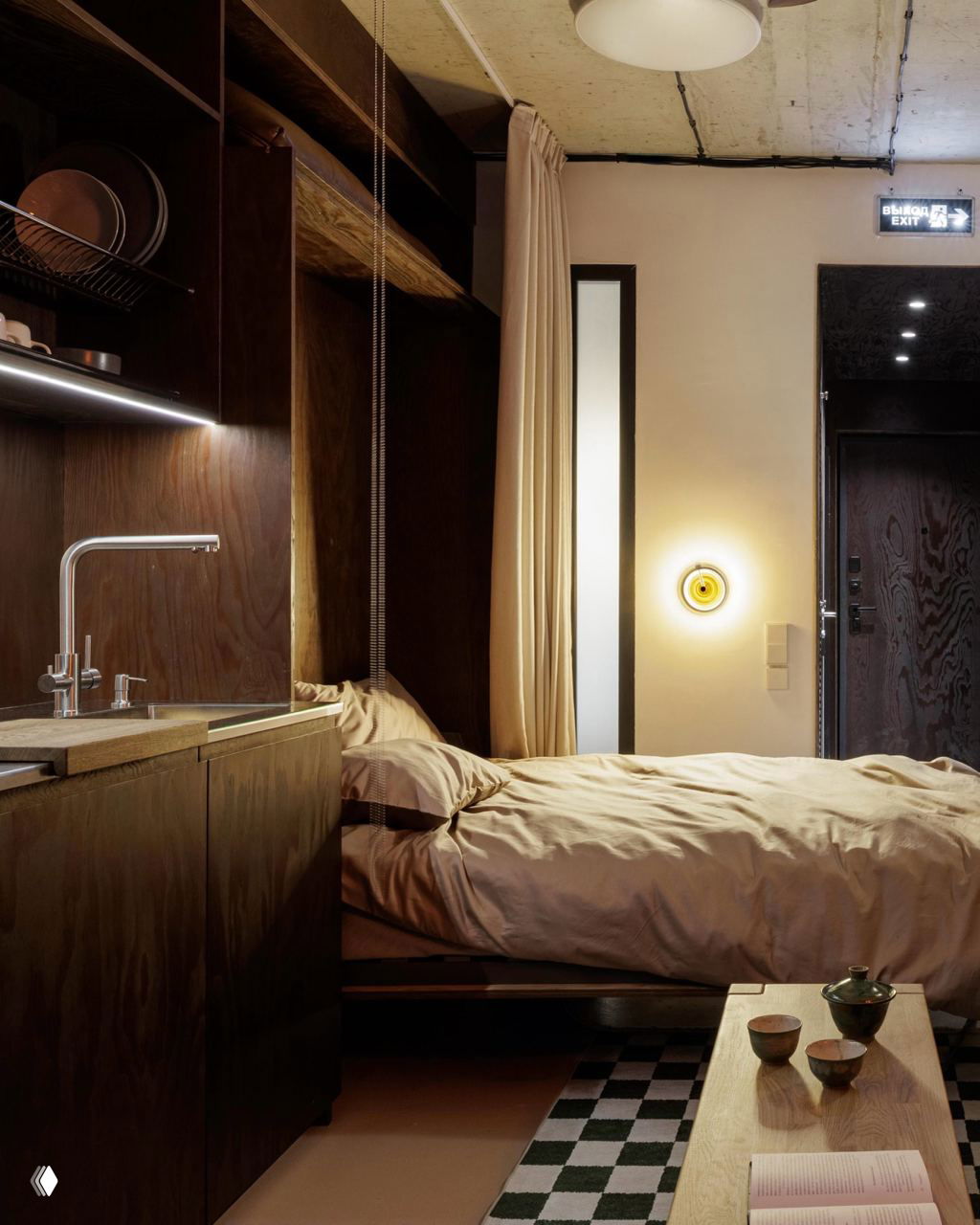 Спальная зона и кухня в одной комнате: опущенная кровать, мягкое освещение, деревянный столик и сдержанная палитра материалов в индустриальном минимализме