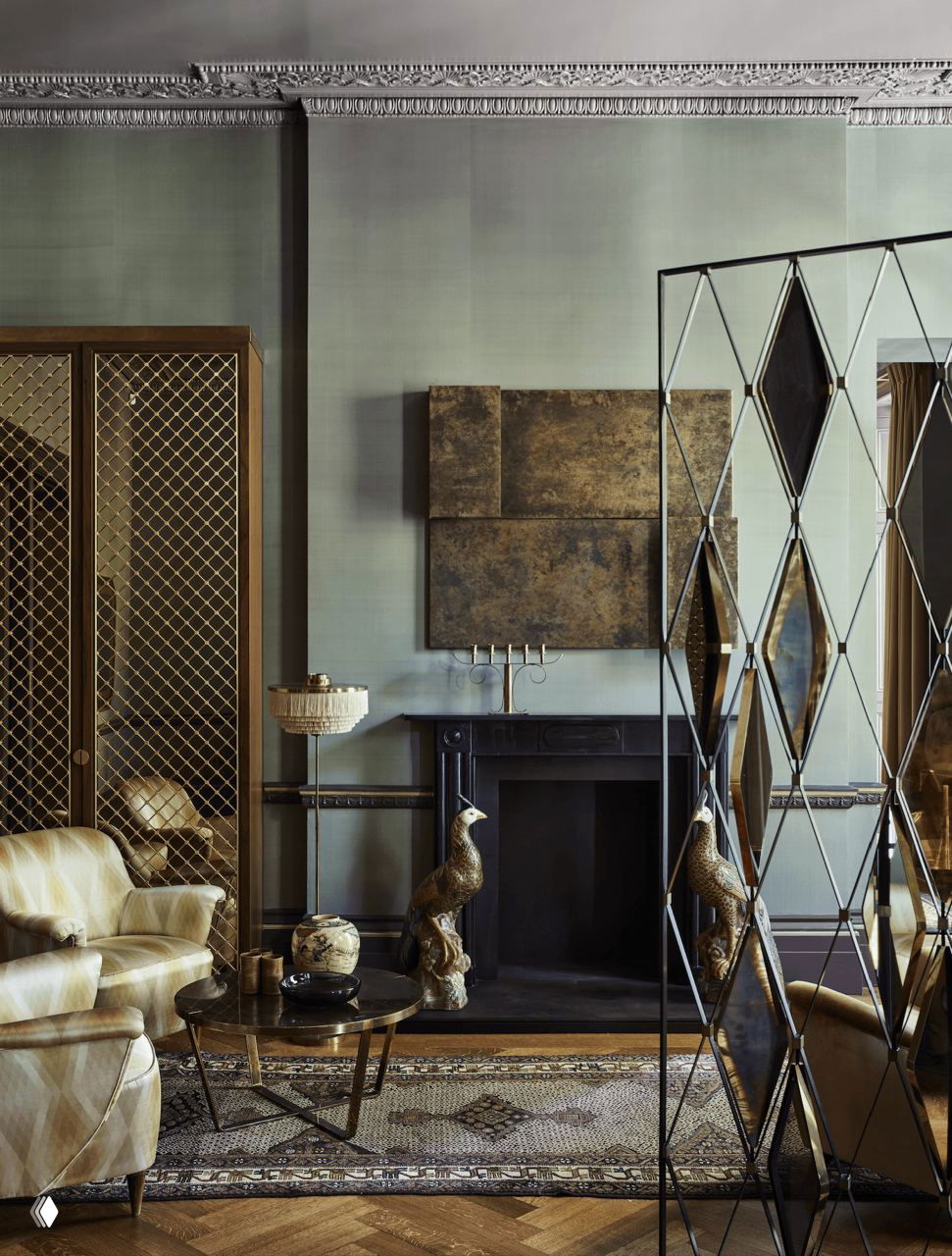 Угол гостиной с камином и декоративными панелями: зелёные тона обоев, антикварная мебель, декоративные скульптуры и зеркало в высокой раме создают музейную атмосферу.