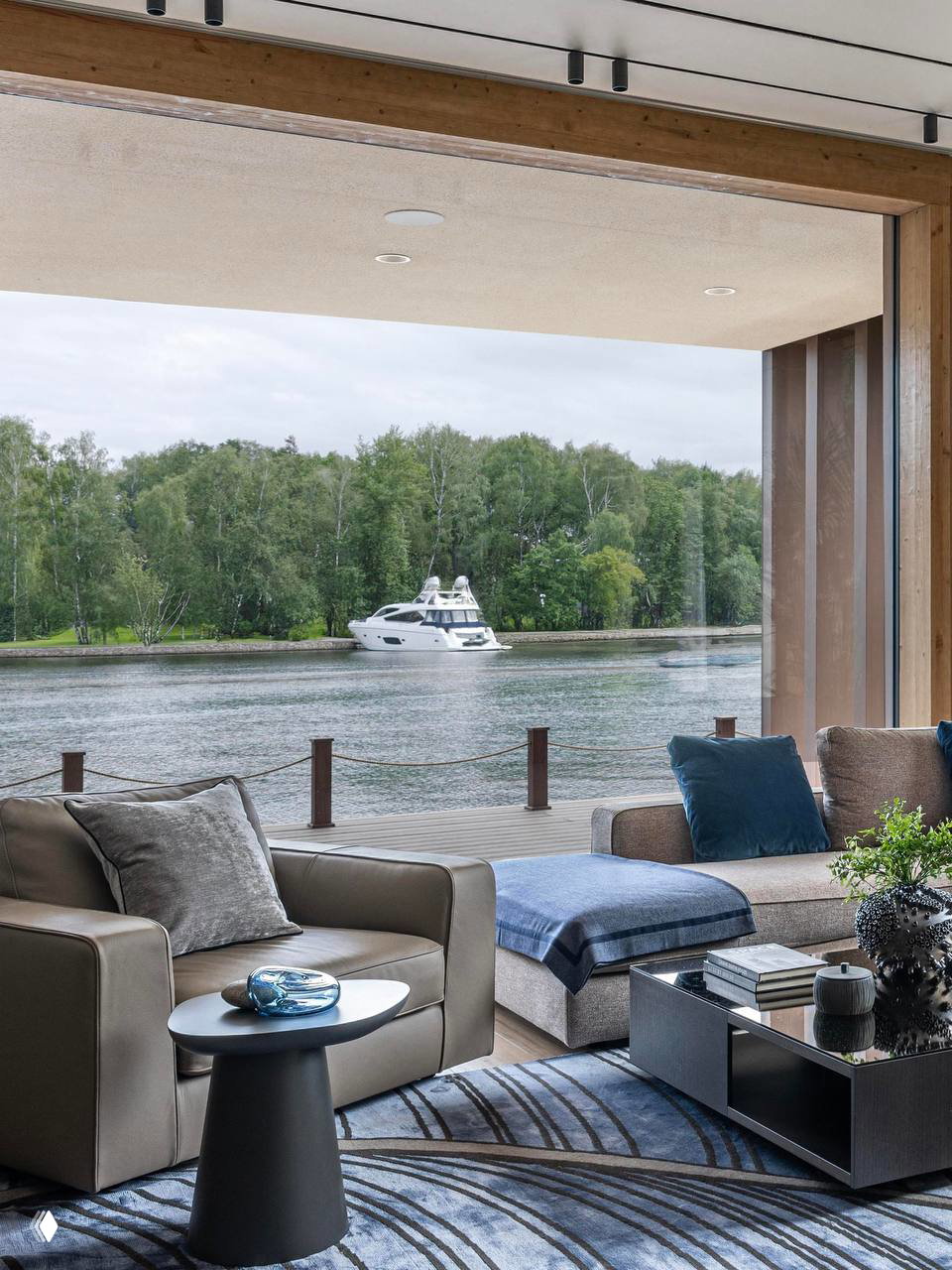Гостиная с панорамным окном на реку: диван, пуф и журнальный столик, вид на причал и лодку; интерьер в натуральной гамме дерева, камня и текстиля.