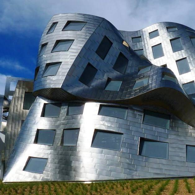 Ближайний план изгибающейся металлической оболочки здания с квадратными окнами — характерный мотив в работах Гери.