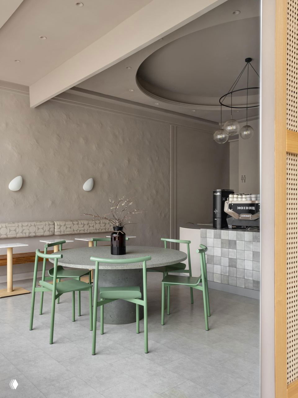 Общий вид зала: круглый стол с зелёными стульями, мягкая скамья и аккуратное освещение — сочетание натуральных текстур и минимализма.