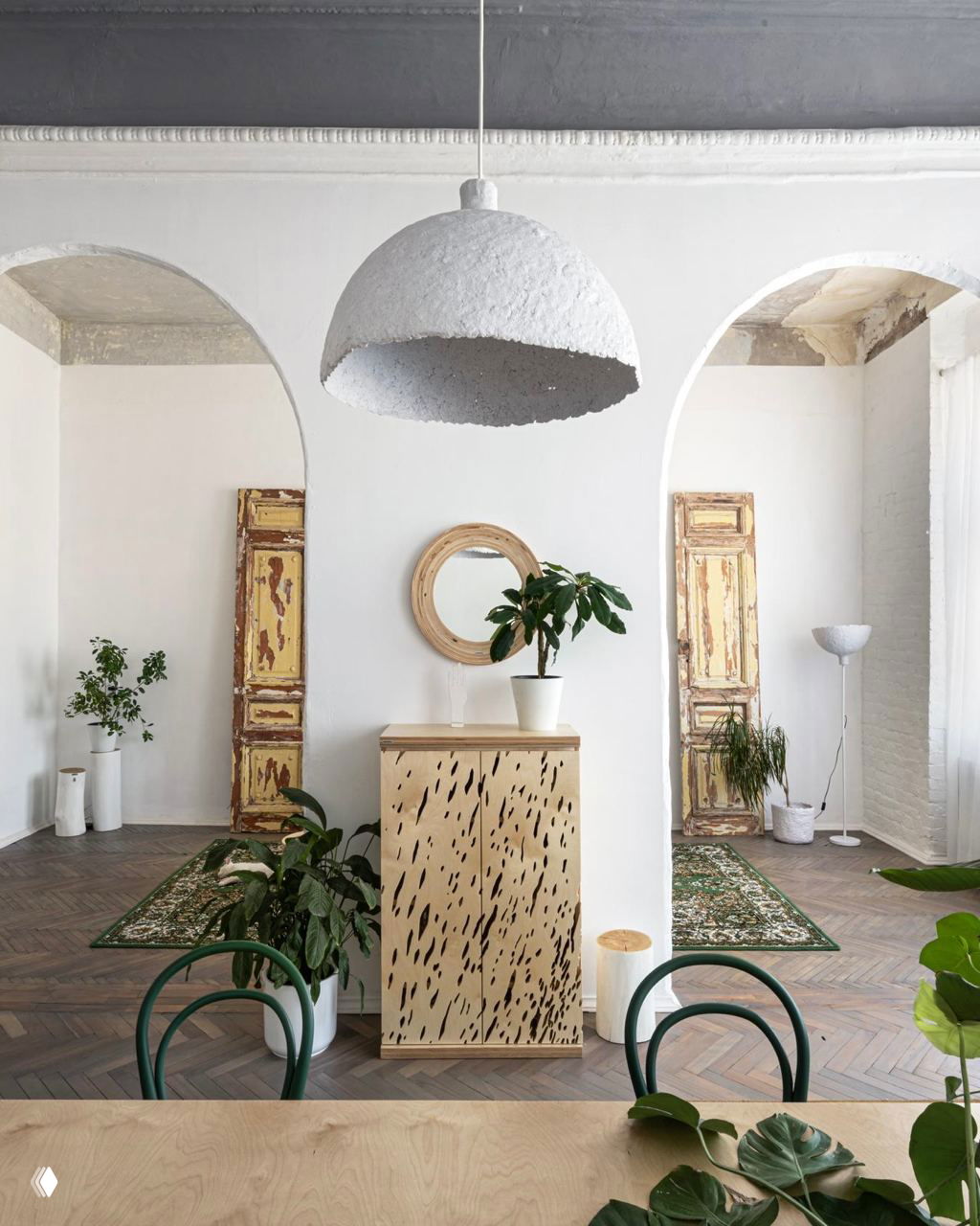 Интерьер с арочными проёмами, белыми стенами и деревянным буфетом на фоне зелёных ковров и комнатных растений, акцент на органичность.
