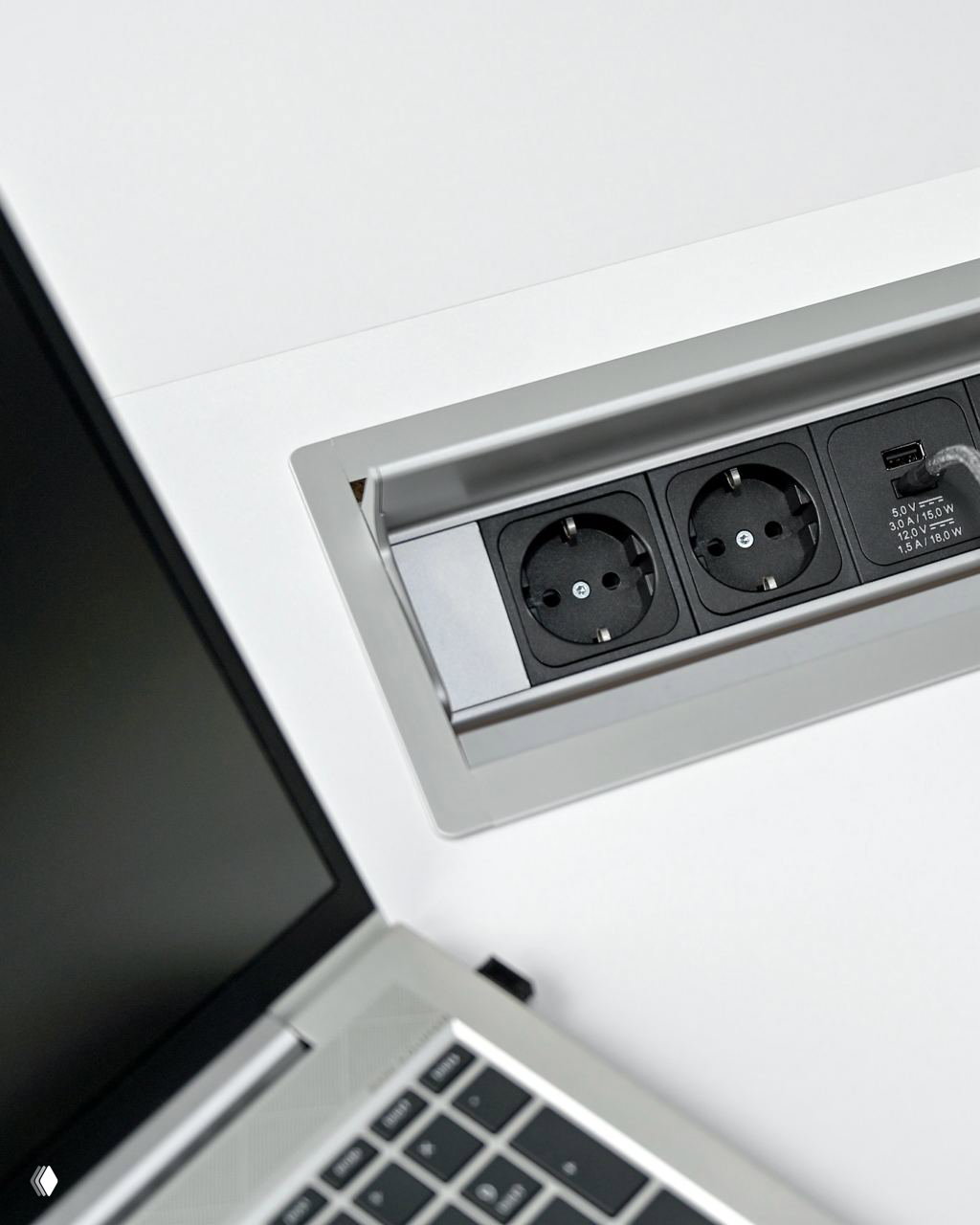 Встроенная выдвижная розетка в столешнице: три силовые розетки и USB-порт рядом с рабочим местом и открытым ноутбуком.