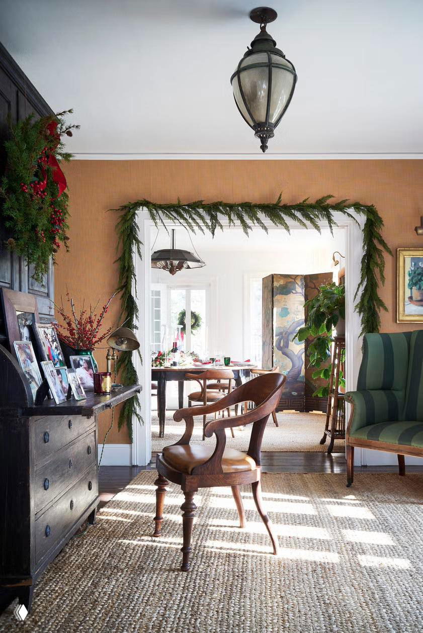 Арка и входная зона, украшенные еловой гирляндой и декоративными элементами; деревянная мебель и естественный свет создают тёплый канцелярский интерьер.