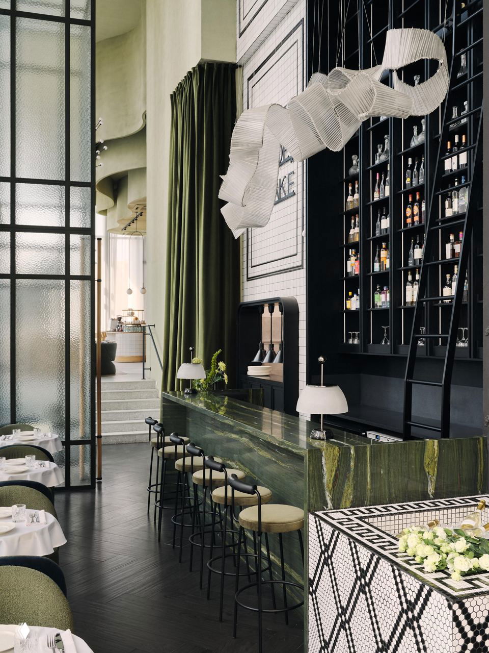 Барная зона Grande Bibliotheca: зелёная мраморная стойка, высокие потолки, тёмные стеллажи с бутылками и барные стулья у стойки.