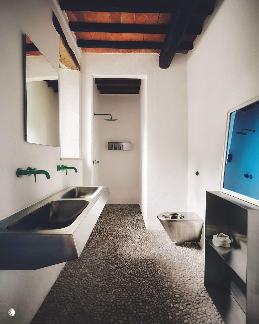 Ванная комната с промышленной сантехникой: стальные раковины и унитаз, пол из речной гальки и небольшие зелёные акценты на смесителях.