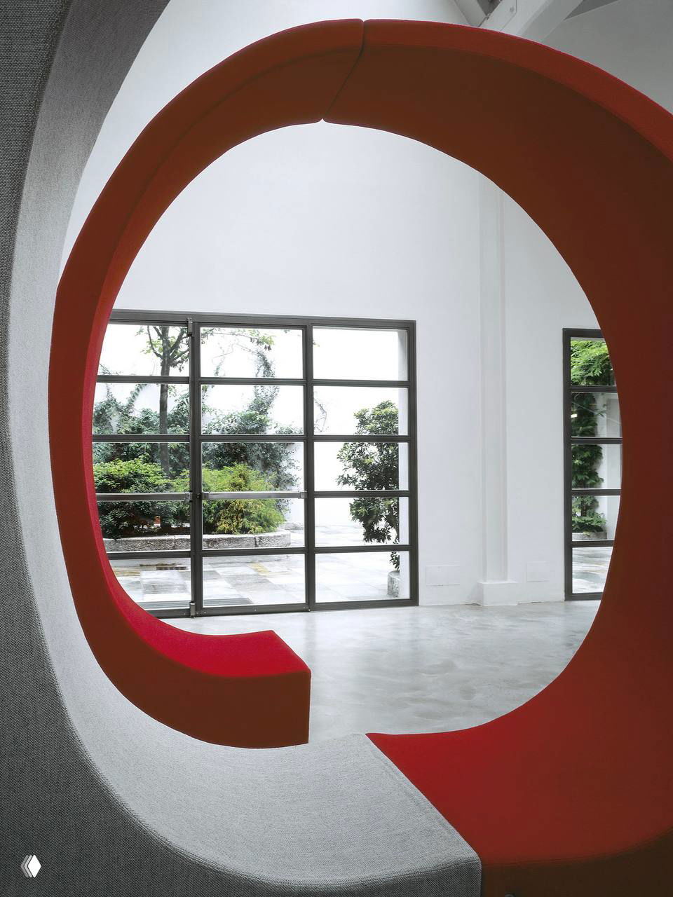 Архитектурный элемент в виде большого круглого проёма с ярко-красной встроенной скамьей на фоне окон во внутренний двор.