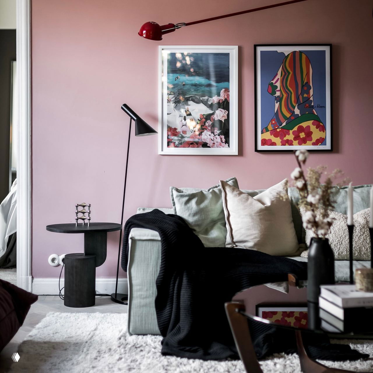 Уютный диванный уголок с розовой стеной, картинами и торшером: светлые подушки, чёрный плед и декоративный столик формируют комфортную атмосферу в гостиной