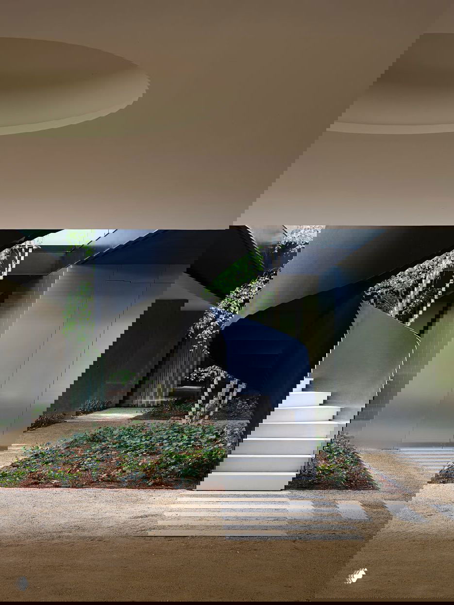 Внутренний двор с чёрной спиральной лестницей, посадками берёз и дорожкой из гравия — переход между корпусами и связь с природой на участке.