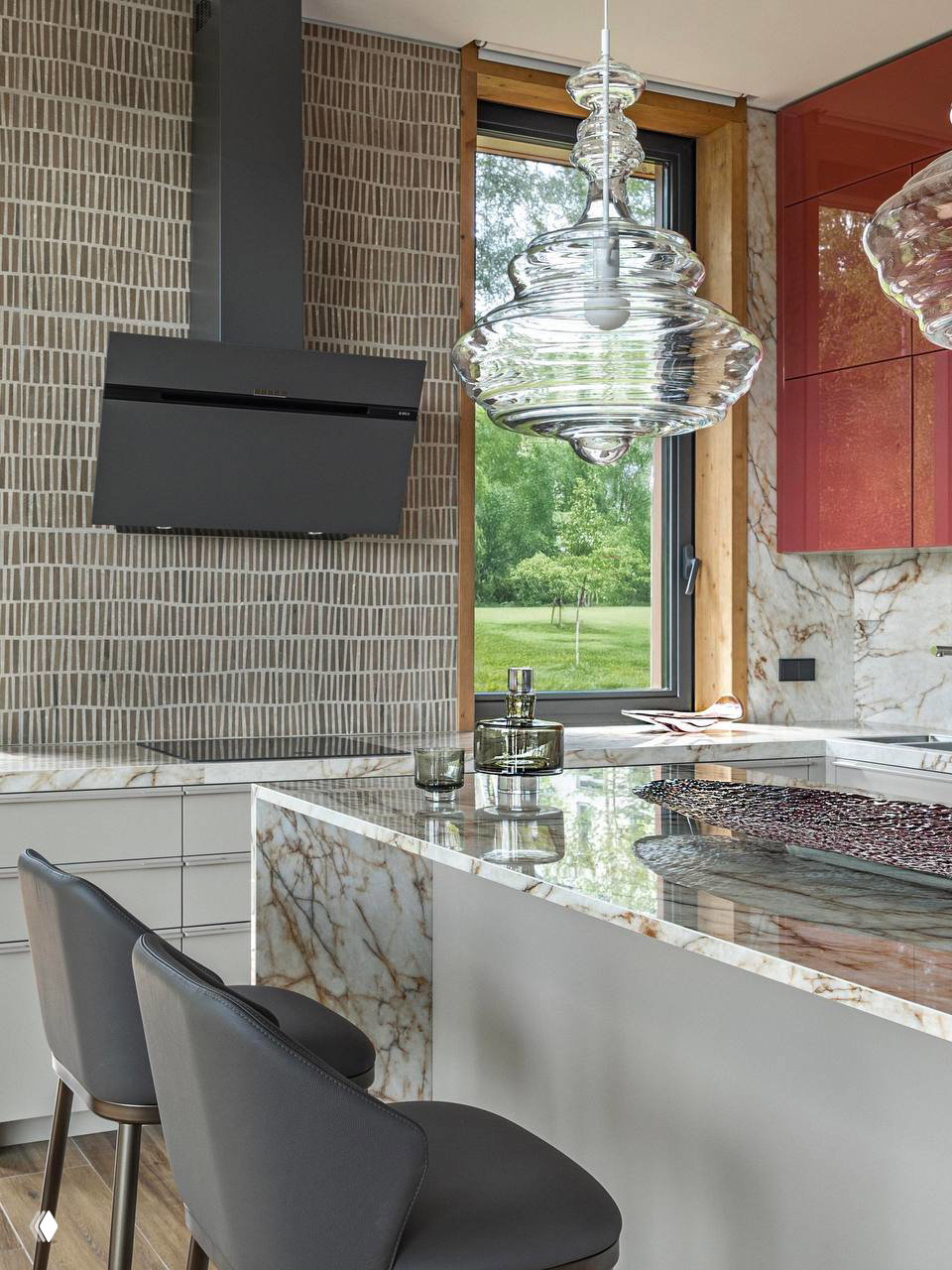 Кухонный остров с мраморной столешницей, барные стулья и стеклянные подвесные светильники; сочетание натурального камня и современного оборудования.