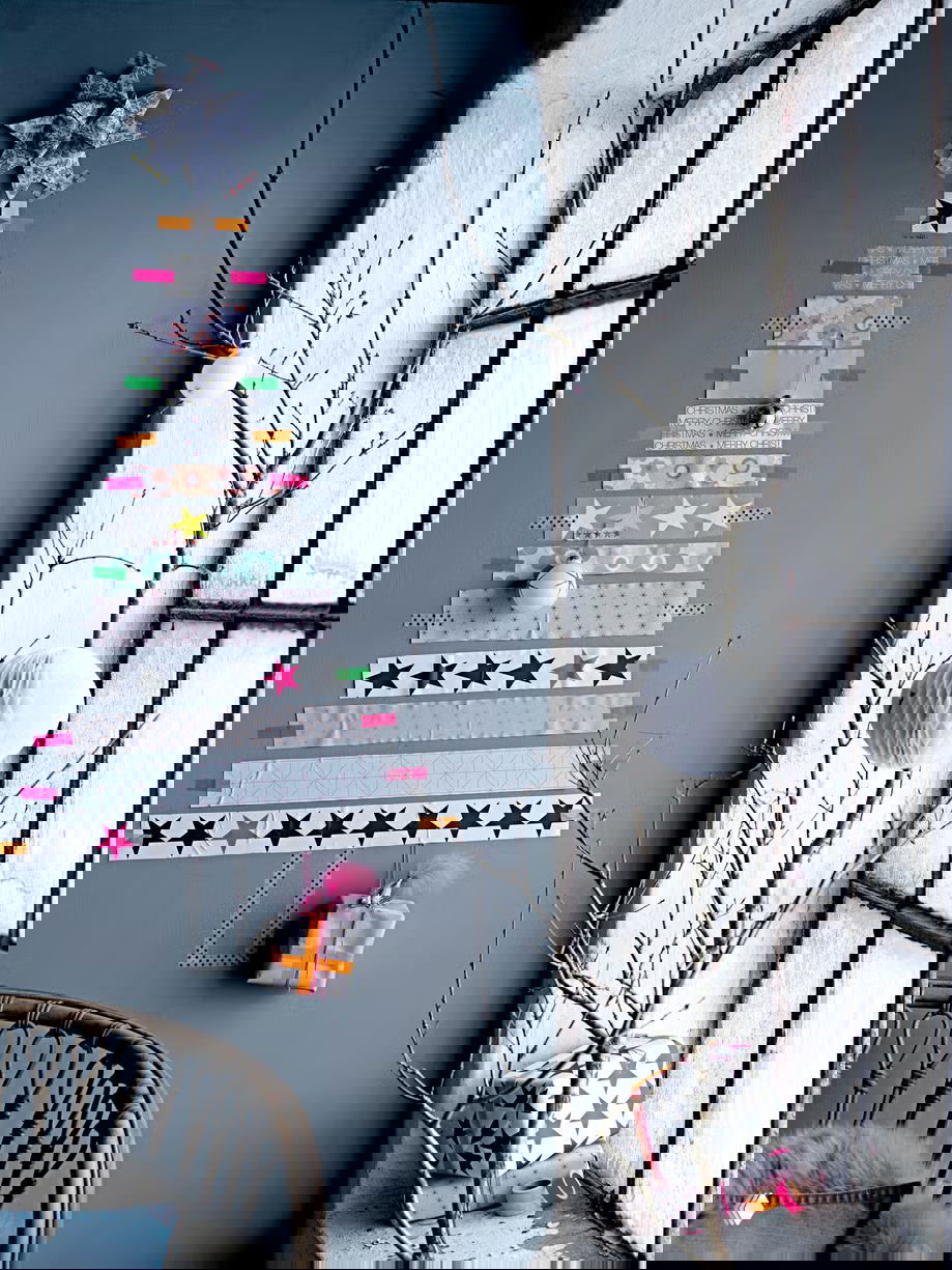 Минималистичная ёлка, составленная из полос декоративного скотча на серой стене, с декоративными шариками и маленьким подарком у подоконника.