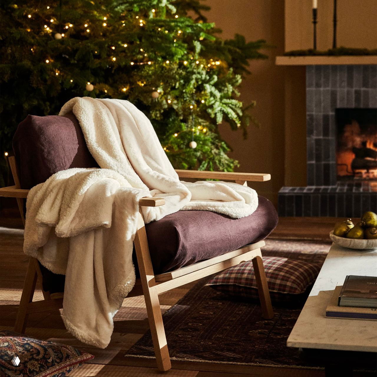 Кресло с пушистым белым пледом на фоне украшенной рождественской ёлки и работающего камина: тёплый зимний интерьер, приглашающий к отдыху и чтению