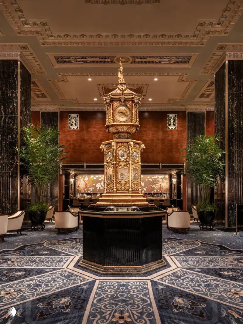 Интерьер лобби с большой центральной декоративной часовой конструкцией, колоннами и элегантной мебелью в классическом стиле отеля.