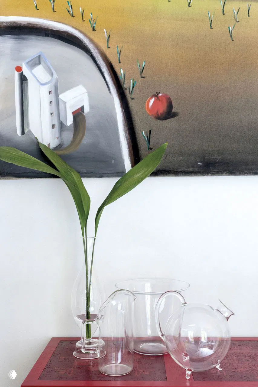 Крупный план стеклянных графинов и вазы на столике перед картиной, подчёркивающий прозрачность и минимализм интерьера микроквартиры.