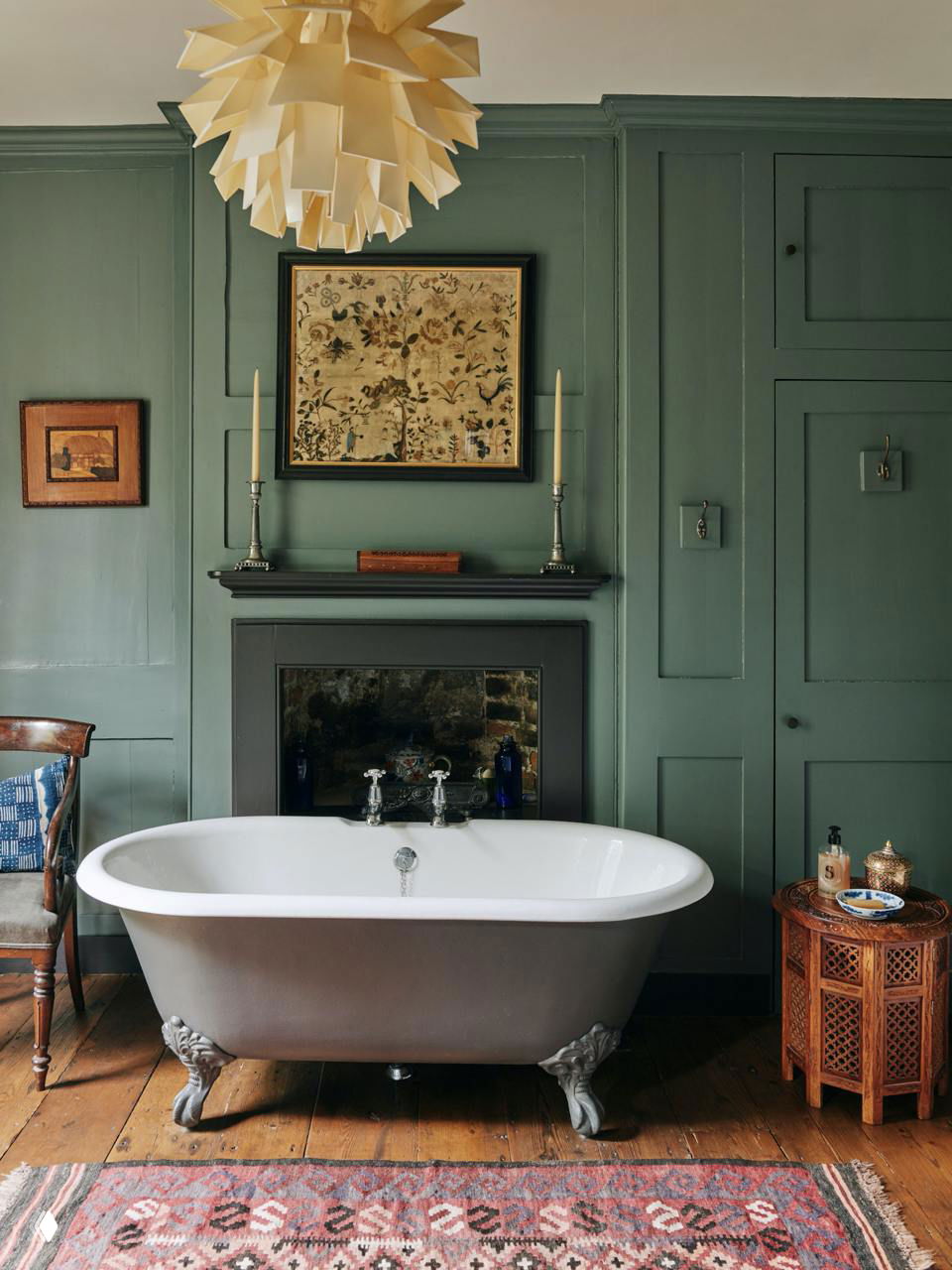 Ванная комната с зелёными панелями в лондонском доме: чугунная отдельностоящая ванна на лапах, деревянный пол, этнический ковёр и настенные украшения в винтажном стиле.