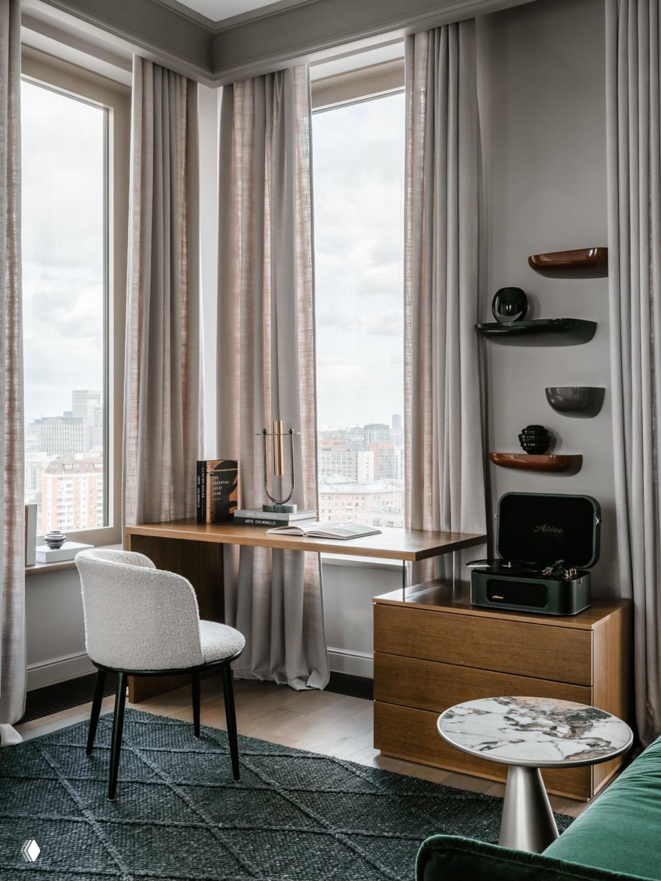 Рабочая зона у панорамного окна: деревянный стол, белое кресло, шторы в пастельных тонах и виниловый проигрыватель, вид на городской пейзаж Москвы.