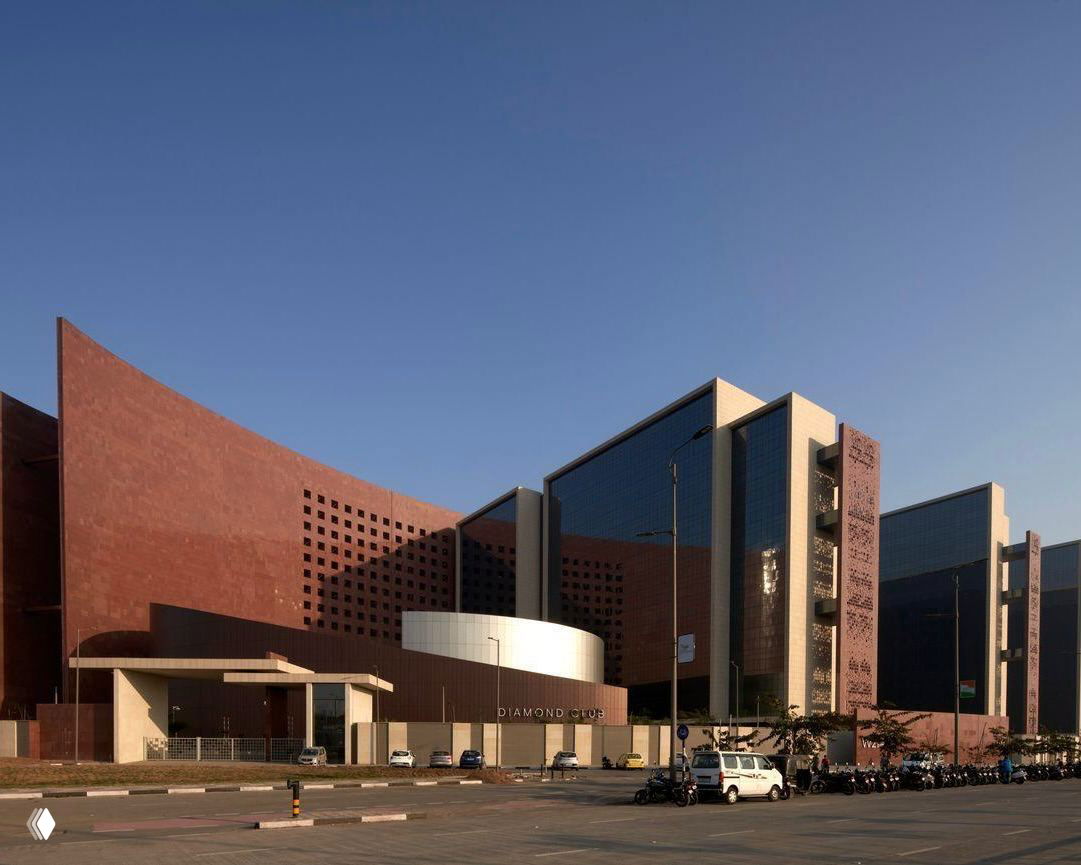 Фасад Биржи алмазов в Индии: крупный современный комплекс с тёмно‑красными стенами, большим остеклением и городским окружением на переднем плане.