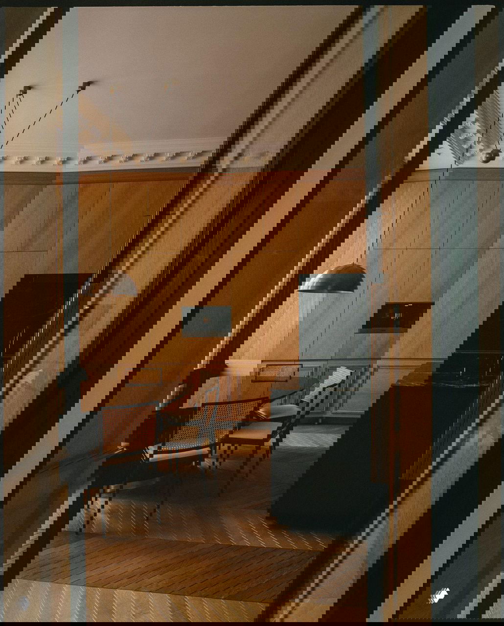 Интерьер с кухонной зоной и обеденным столом: панельные деревянные стены, канонический паркет и минималистичная чёрная мебель в парижском доме барона Османа.