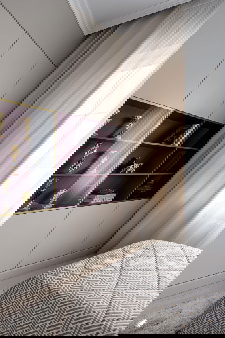 Спальня или гостевая с текстильной отделкой и встроенными шкафами, фотографии трофеев и нейтральные шторы создают домашнюю атмосферу.