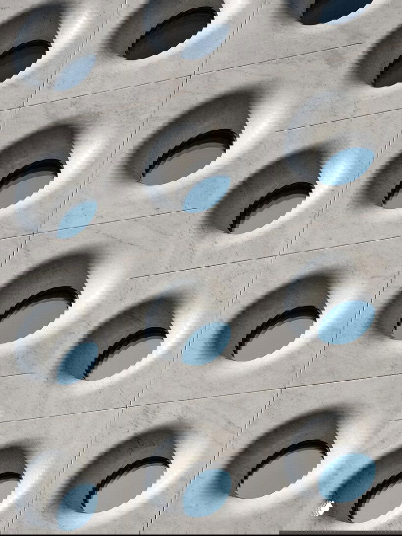 Крупный план каррарского мрамора с углублёнными круглыми проёмами‑окнами, подчёркивающими текстуру и игру света на поверхности фасада.