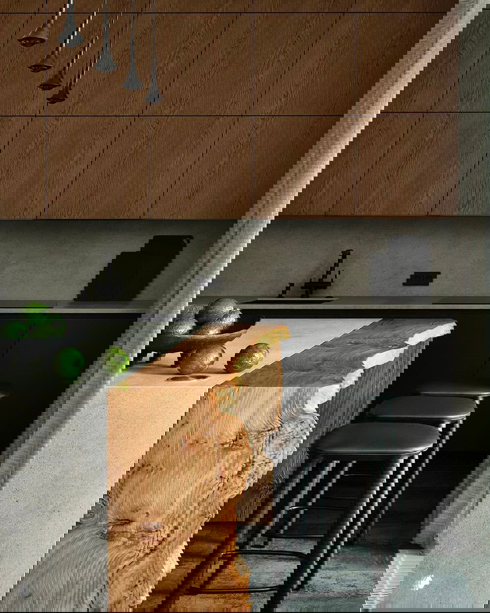 Темная стильная кухня с массивной деревянной кромкой острова из цельного среза дерева, барными стульями и строгими фасадами шкафов.