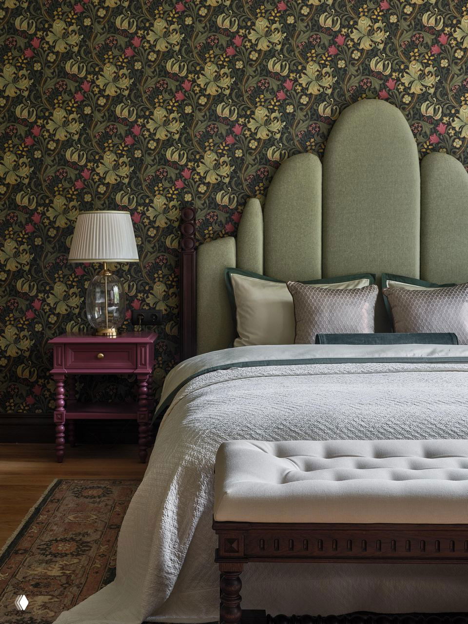 Спальня в английском стиле: высокая мягкая зелёная спинка кровати, цветочные обои и текстиль в спокойных тонах, декоративные тумбочки и лампа.