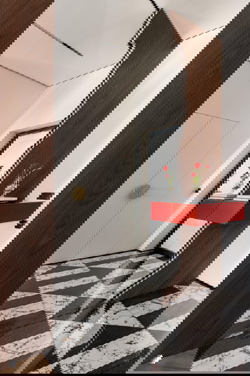 Прихожая с декоративной деревянной перегородкой, красным подвесным консольным столом и чёрно‑белой мраморной геометричной плиткой на полу.