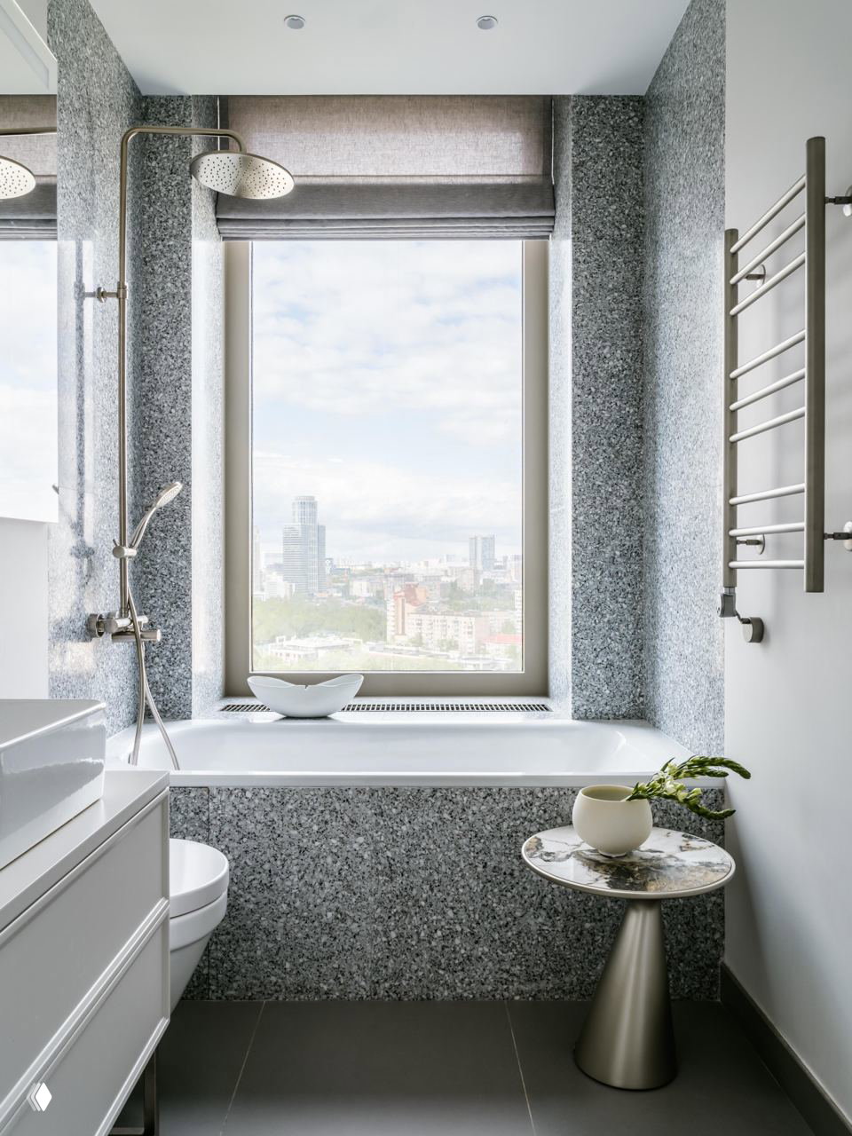 Ванная комната с окном и ванной у подоконника: стеновые панели с фактурной плиткой, хромированная сантехника и маленький мраморный столик с растением.