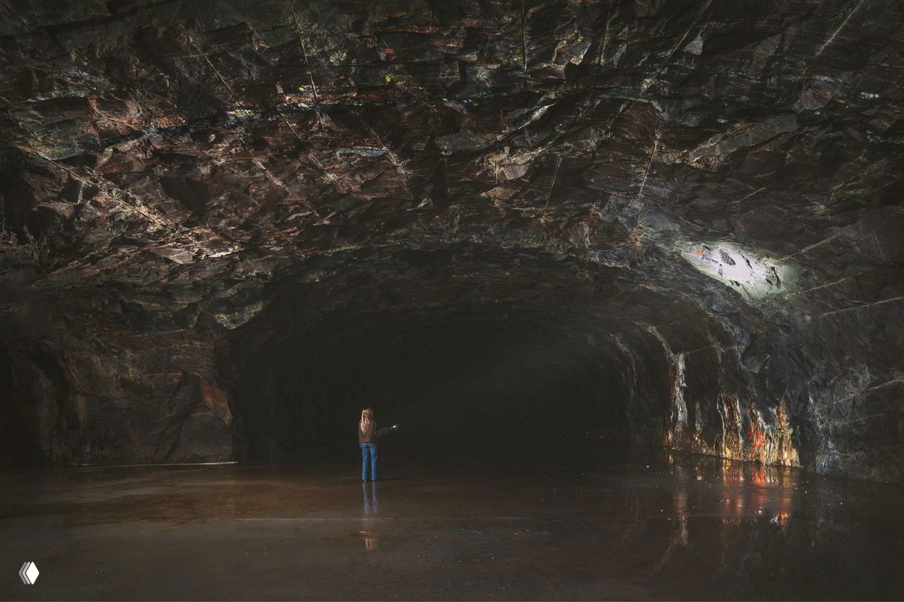 Панорамный вид большой камеры пещеры с отражающим полом; человек вдалеке даёт представление о масштабе и внушительности подземного объёма.