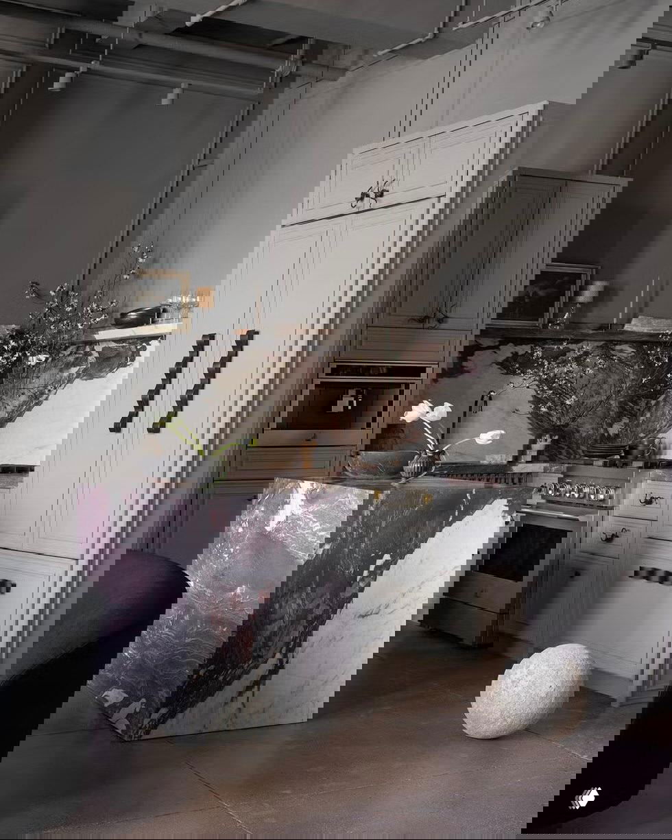 Лаконичный интерьер с тёмно-серыми и мраморными акцентами, кубическим островом из камня, высоким пространством и художественной темной стеновой росписью.