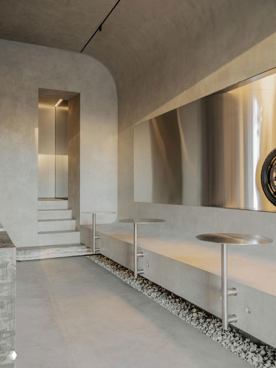 Мотоцикл, выставленный как экспонат внутри кофейни, на фоне зеркальных стальных панелей и бетонных поверхностей — элемент райдерской эстетики.