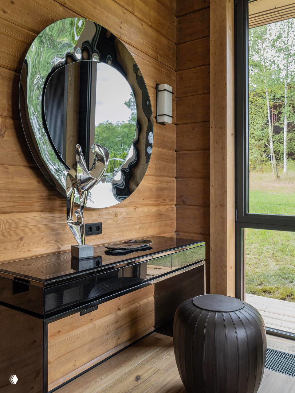 Прихожая с круглым декоративным зеркалом и консолью на фоне деревянной стены; акцент на отражениях и текстуре древесины в интерьере.