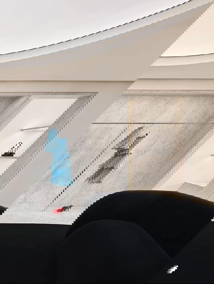 Часть пространства с круглыми потолочными нишами, подвешенным голубым платьем и красными туфлями — яркие акценты на нейтральном мраморном фоне.