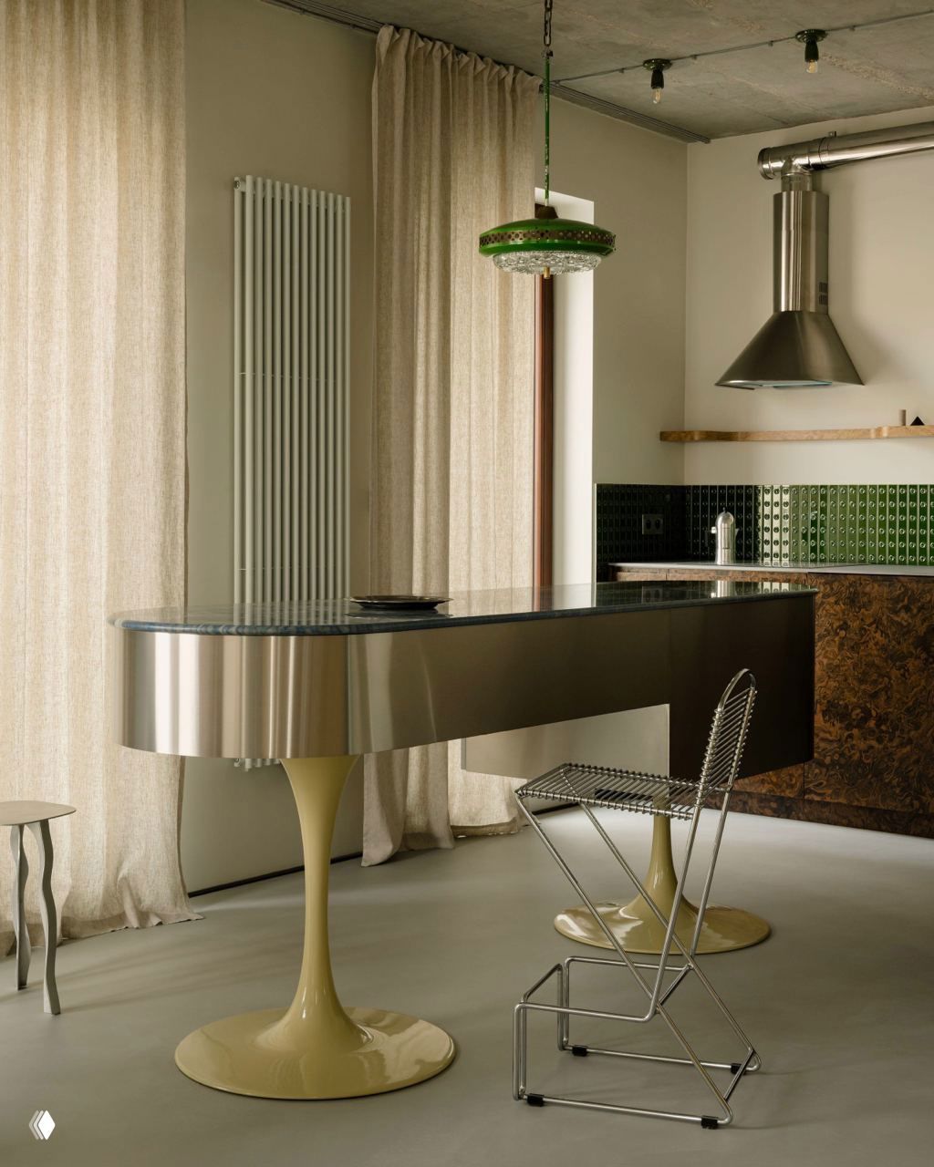 Авангардный кухонный остров с глянцевой металлической столешницей на опорах-пьедесталах, рядом легкие стулья и мягкие шторы на фоне.