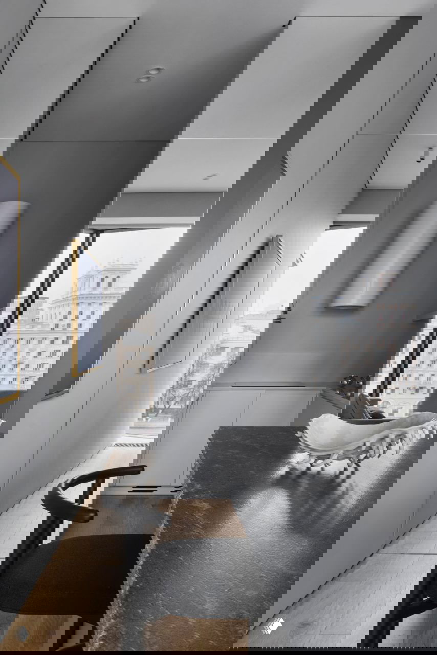 Узкий проход-кухня в спокойной серой гамме: гладкие фасады, цилиндрическая вытяжка и продолжение тёмной столешницы в минималистском решении интерьера.