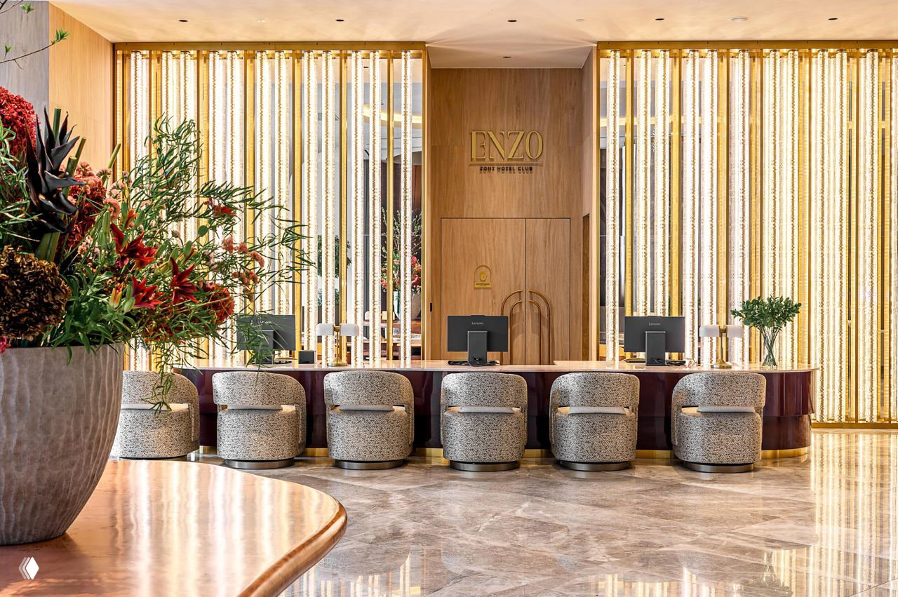 Ресепшн отеля Enzo Hotel Moscow: мраморный пол, мягкие кресла у стойки регистрации и вертикальные золотые световые элементы за стойкой.