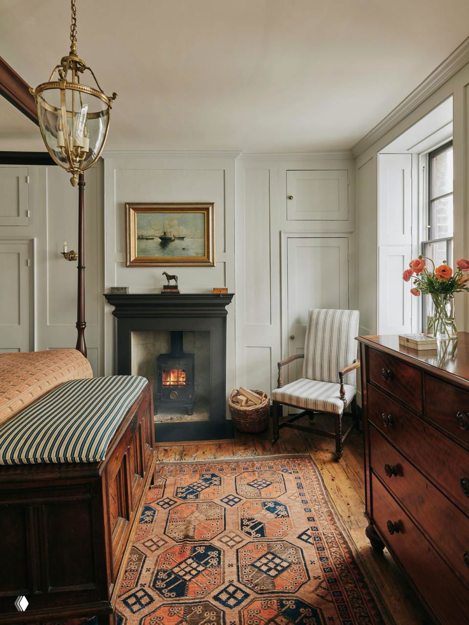 Спальня с маленькой печью вместо камина, деревянной мебелью и ярким ковром: интерьер напоминает атмосферу загородного поместья в центре Лондона, с собранными владельцем антикварными вещами.