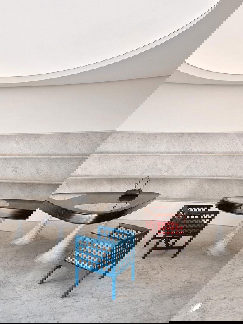 Круглые мраморные тумбы и пол в торговом зале; деревянные и окрашенные стулья на фоне волнообразной мраморной стены, подчёркивающие скульптурность зон.