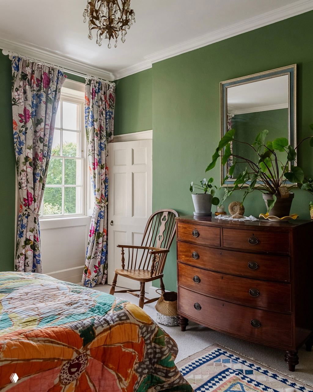 Уютная спальня с зелёной окраской стен, винтажными шторами и комодом, на котором расположены горшечные растения как декоративный акцент.