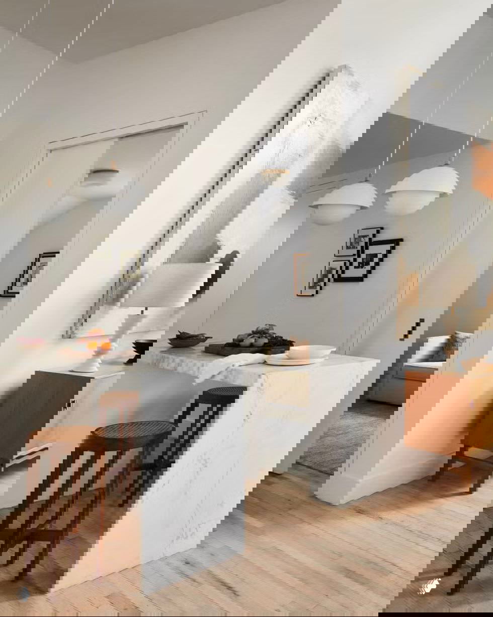 Классический кухонный остров из дерева с тёмной столешницей, плодами и хлебом на поверхности, окружённый подвесными светильниками и шкафами.